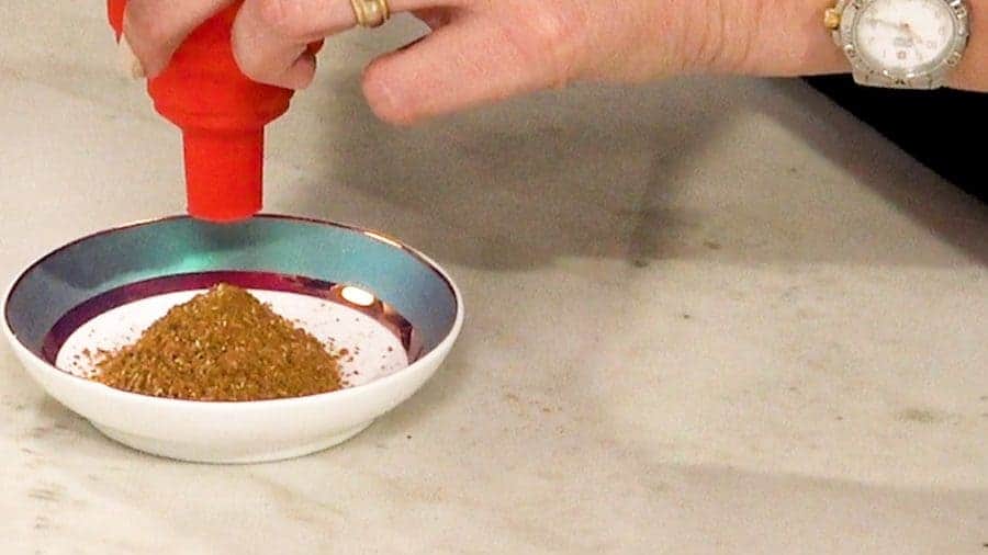 Close up of person using a funnel to pour garam masala in a bowl.
