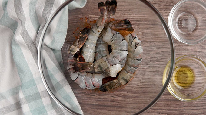 Overhead shot of shrimp in a mixing bowl with the seasoning and oil.