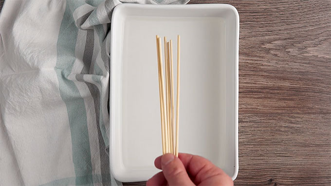 Overhead shot of placing the wood skewers into a pan filled with water.