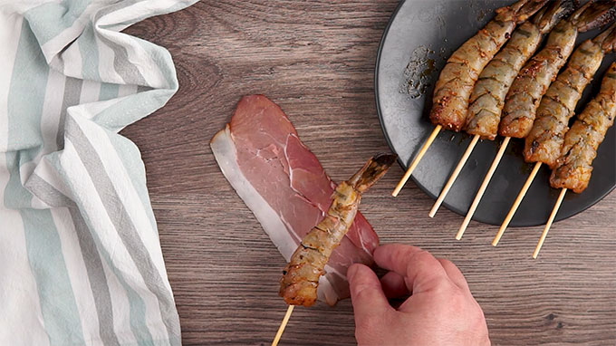 Overhead shot of setting the skewered shrimp on a piece of prosciutto.