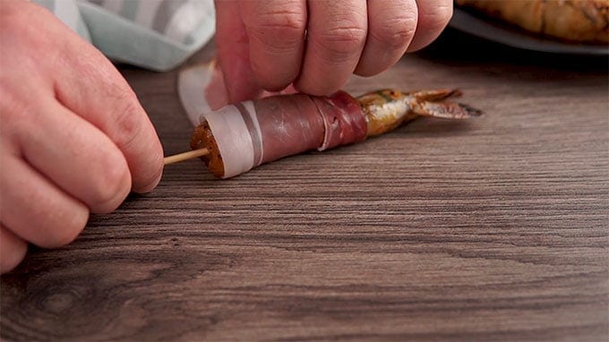 Side shot of wrapping the skewered shrimp in prosciutto.