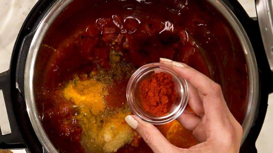 Overhead shot of placing tomatoes and all spices in the bottom of the Instant Pot.