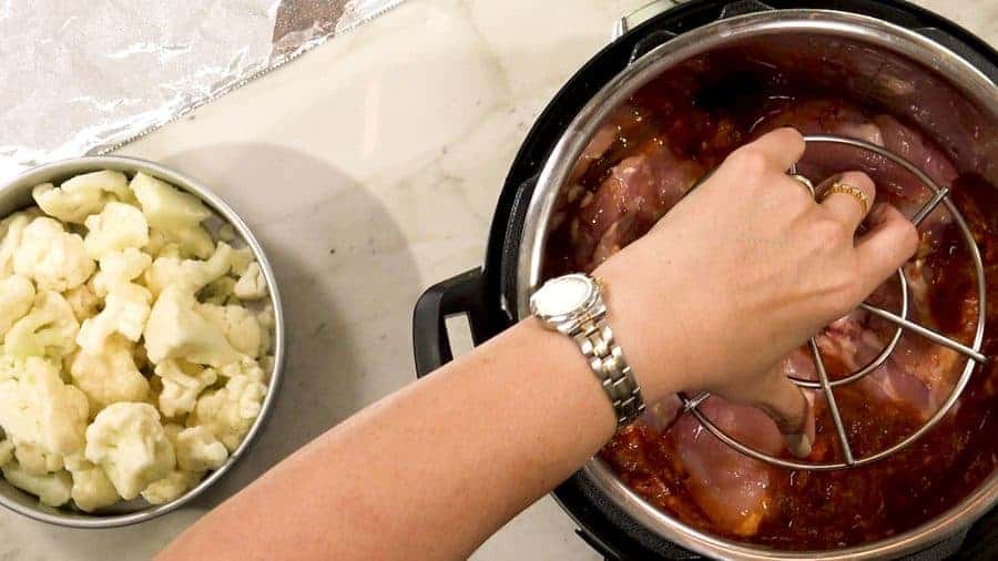 Placing a metal trivet on top of the chicken and sauce.