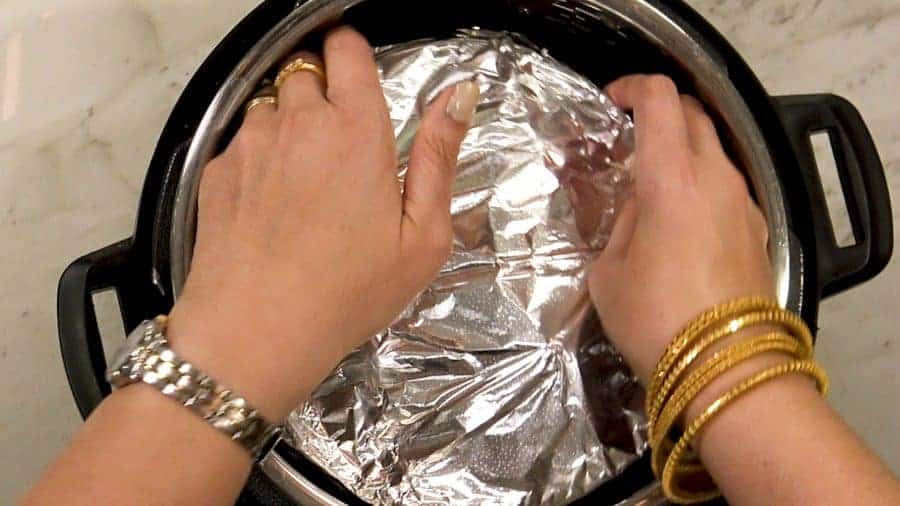 Overhead shot of placing foil covered cauliflower pot on top of the butter chicken in the Instant Pot.