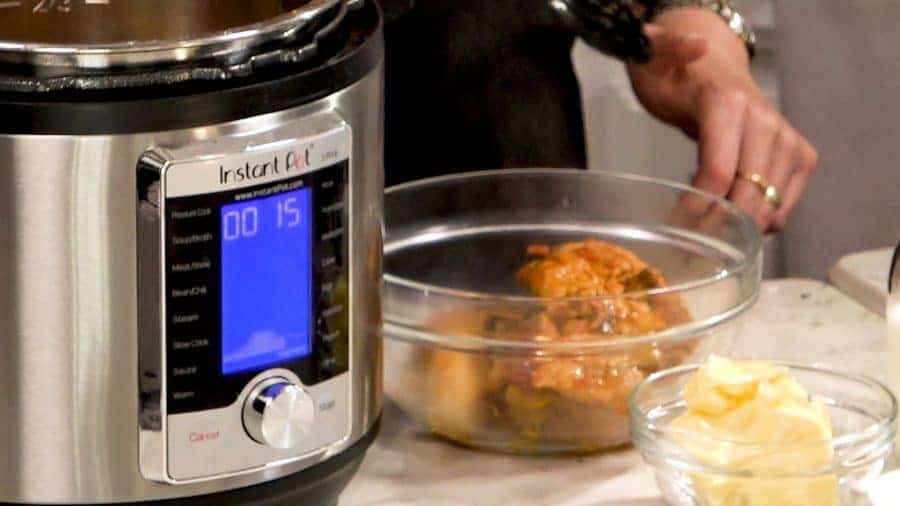 Side view of cooked chicken being removed from the Instant Pot. Sauce left behind.