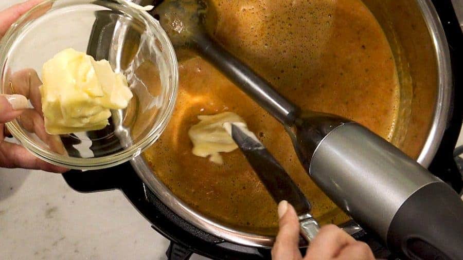 Overhead shot of hand blender mixing in the cream and butter into sauce.