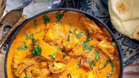 Butter Chicken served in a navy bowl with a side of naan