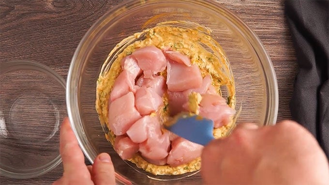 Chicken bites being added to a bowl of spiced yogurt