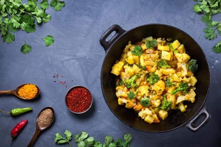 Indian Aloo Gobi dish with potato, cauliflower and spices on the textured grunge background