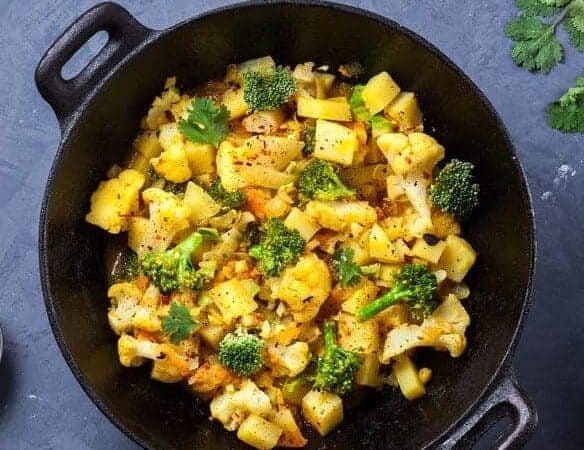 Indian Aloo Gobi dish with potato, cauliflower and spices on the textured grunge background