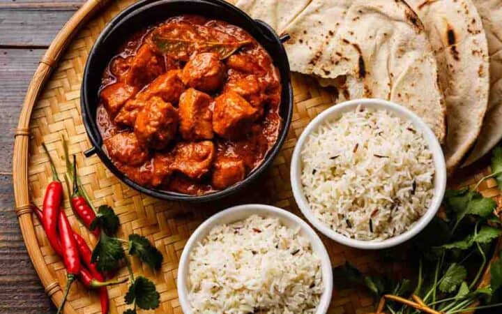 Chicken tikka masala spicy curry meat food in cast iron pot with rice and naan close up