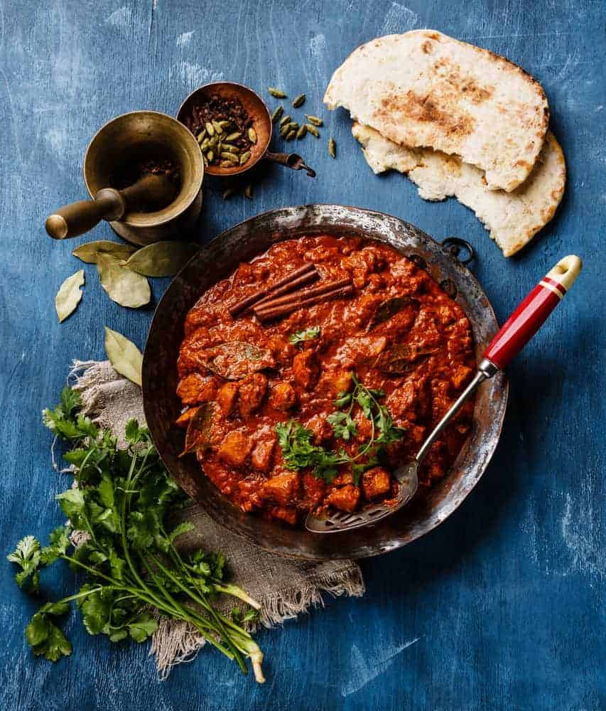 Chicken tikka masala spicy curry meat food in copper pan with naan bread on blue wooden background