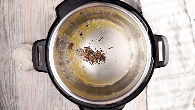overhead shot of instant pot with ghee and cumin seeds