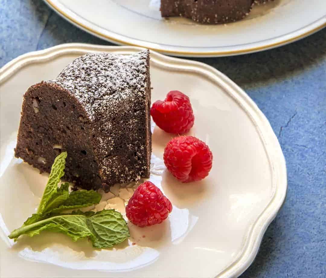 Keto Chocolate Cake on a white plate with raspberries and mint.