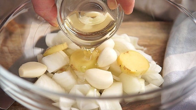 Side shot of the onions, garlic, ginger and oil added to a microwave safe bowl.