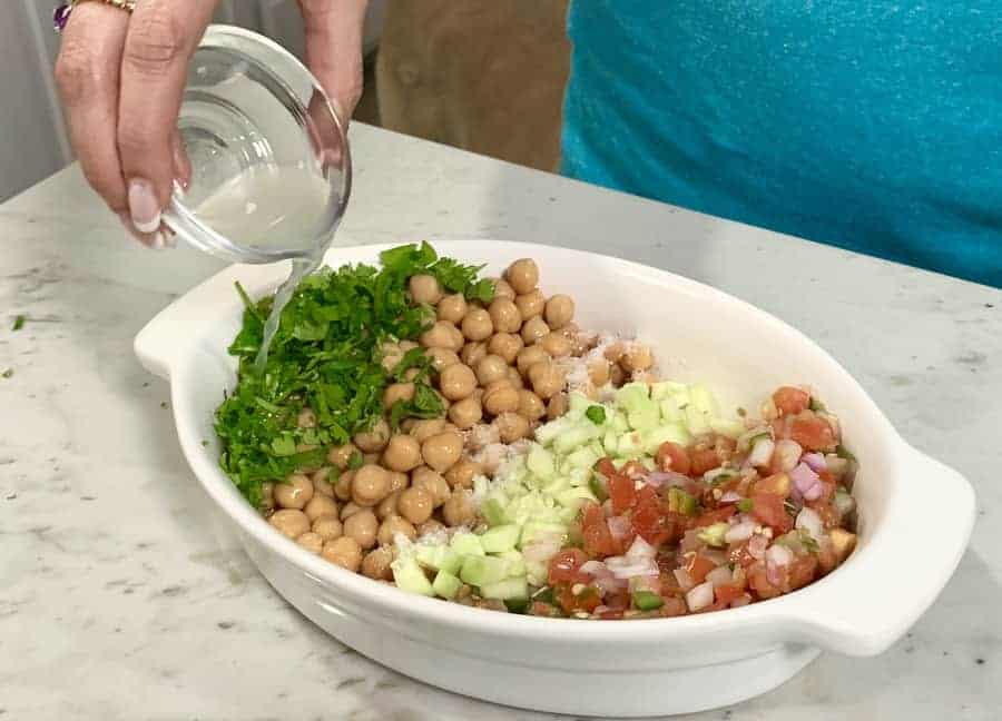 Chickpea salad in a white bowl with lemon juice being poured on it