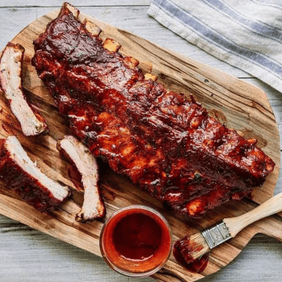 Smoked ribs on a wooden cutting board with bbq sauce and a basting brush