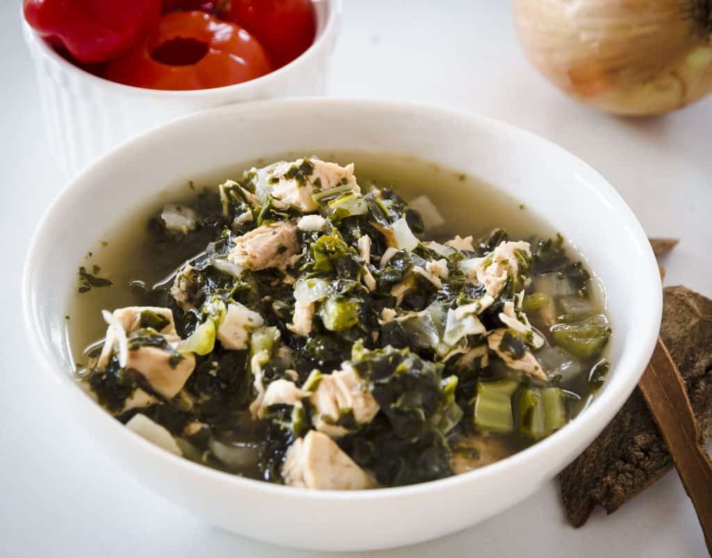 overhead shot of low carb chicken kale soup with red peppadew peppers in the background