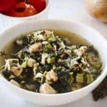 overhead shot of low carb chicken kale soup with red peppadew peppers in the background