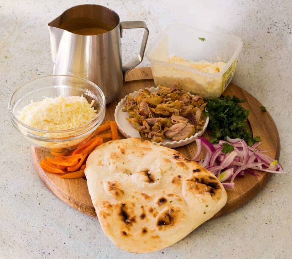 Ingredients for making butter chicken pizza on a board 