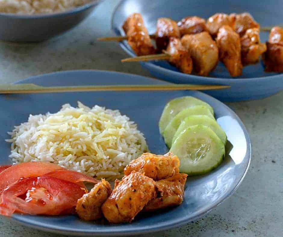 Brochetas de pollo Persas sin pincho en un plato azul con lados de pepino, arroz y tomate fresco