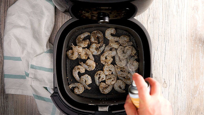 spraying breaded shrimp with oil while in the air fryer