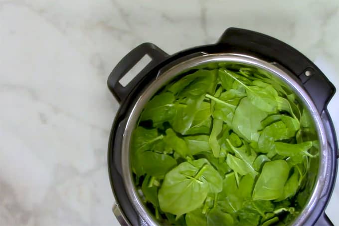 Overhead shot of adding the spinach on top of the other ingredients in the Instant Pot.