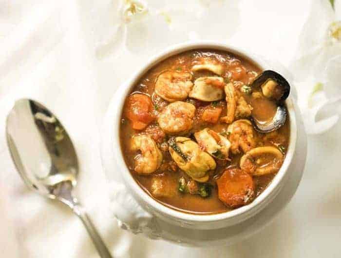 Cioppino Seafood Stew in a white bowl with a spoon on the side