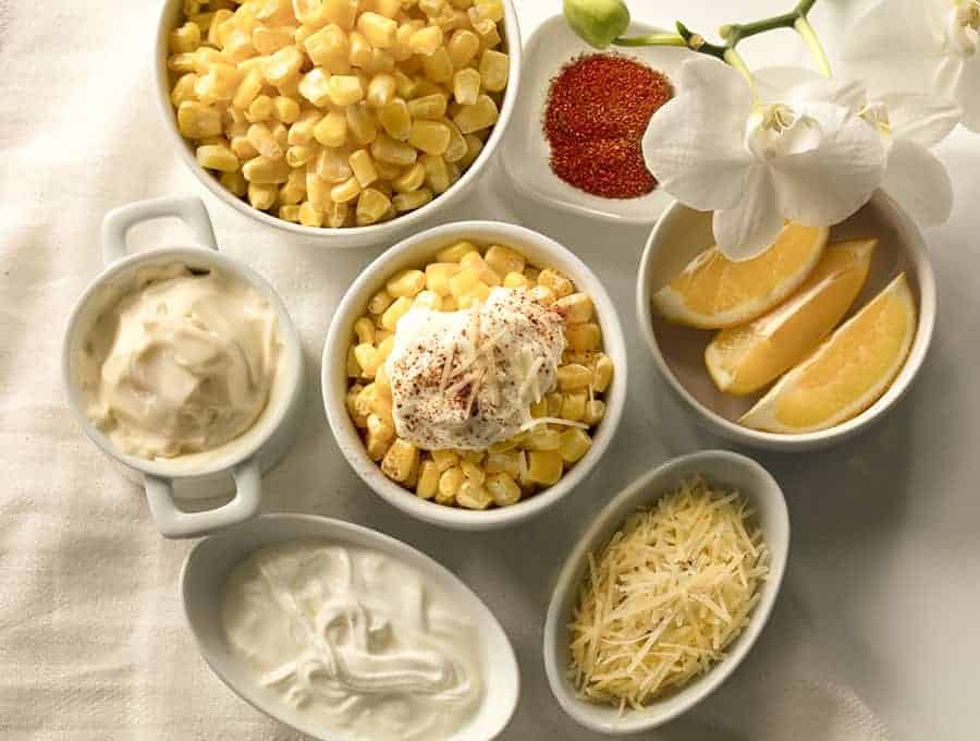 Bowls filled with different types of food on a table including lemons, cheese, dips and corn.