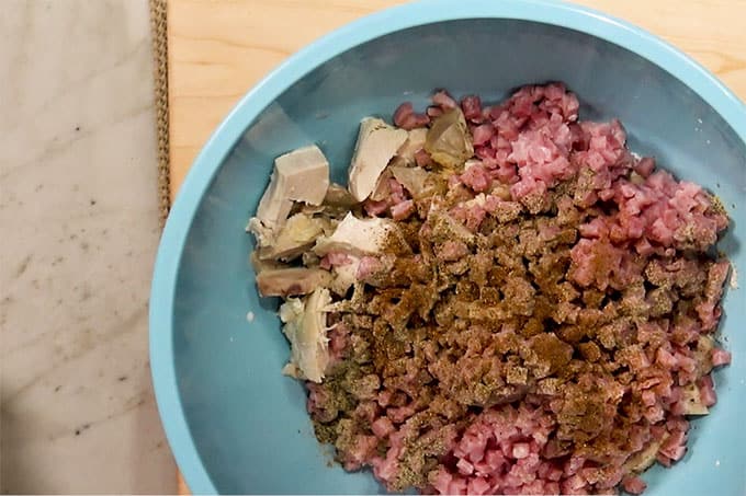 Overhead shot of chicken, ham, pepper, nutmeg and half and half in a mixing bowl.