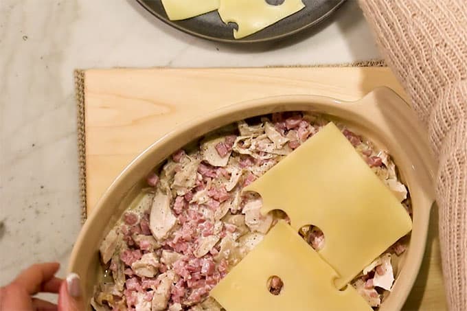 Overhead shot of half the chicken and ham mixture in the pan with swiss cheese slices on top.