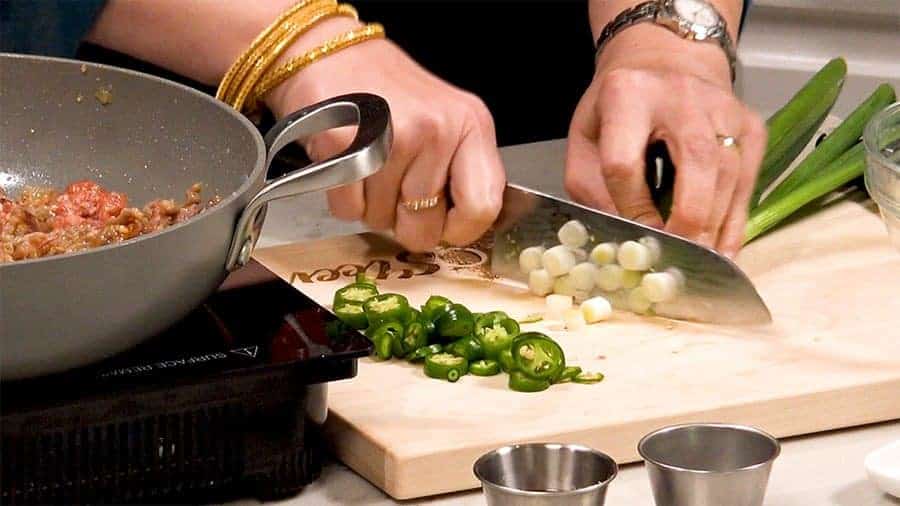 Side shot of chopping green onions and chilis.