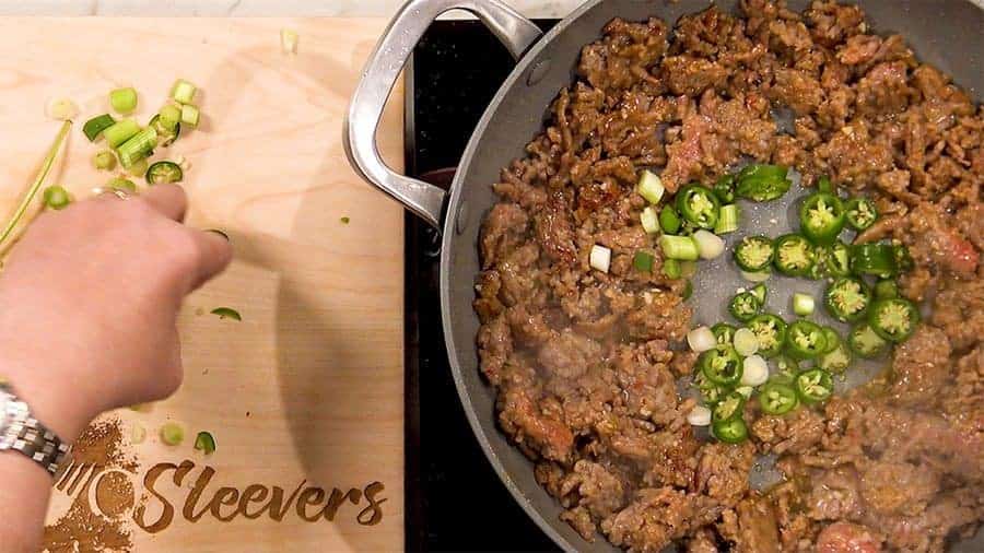 Overhead shot of adding green chilis to center of pan with the ground pork.