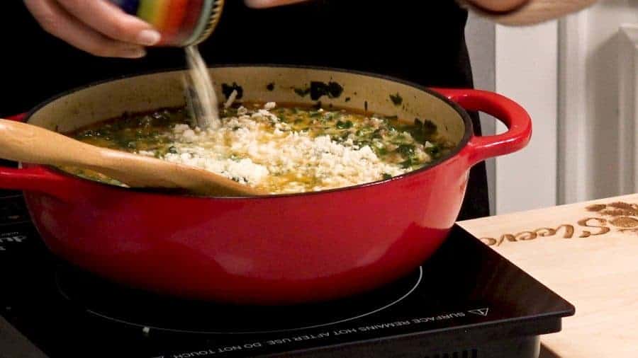 Pouring cream and cheese into a red pot full of soup.