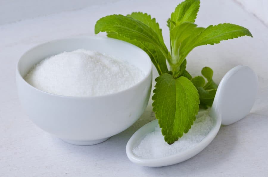 A bowl of Stevia Sweetener with Stevia leaves beside it.