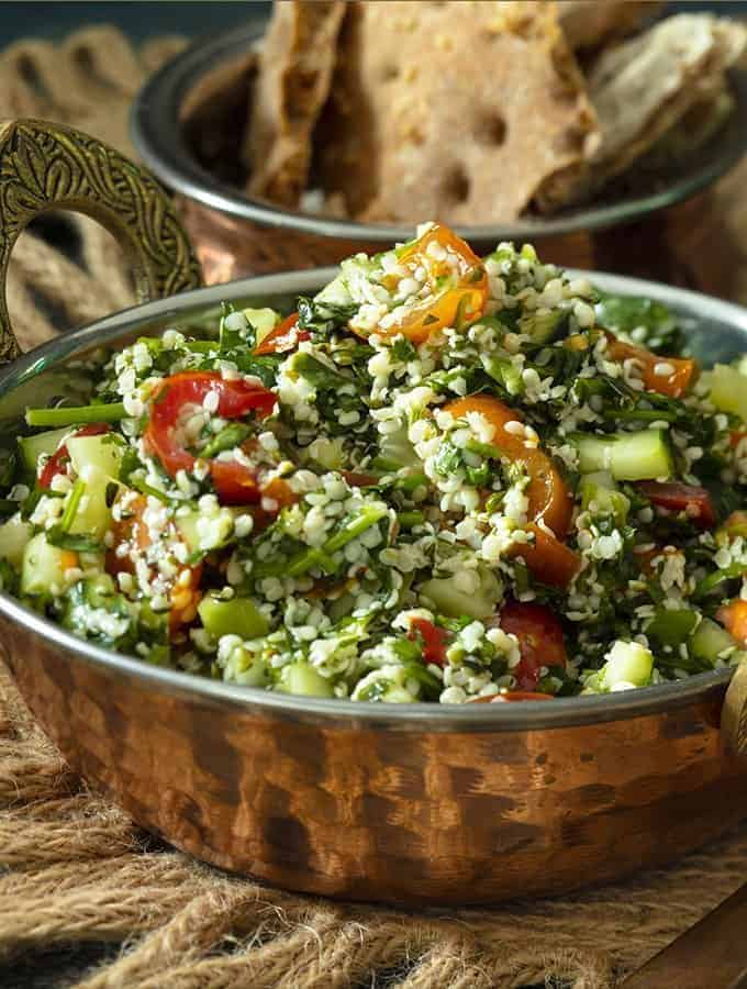 sideways view of tabouli in a brass bowl with crackers in the background