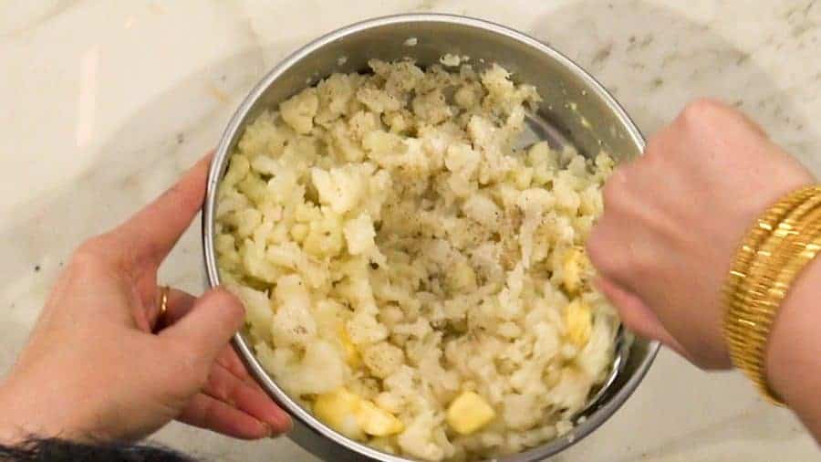 Overhead shot of mashing cauliflower with salt, pepper and butter.