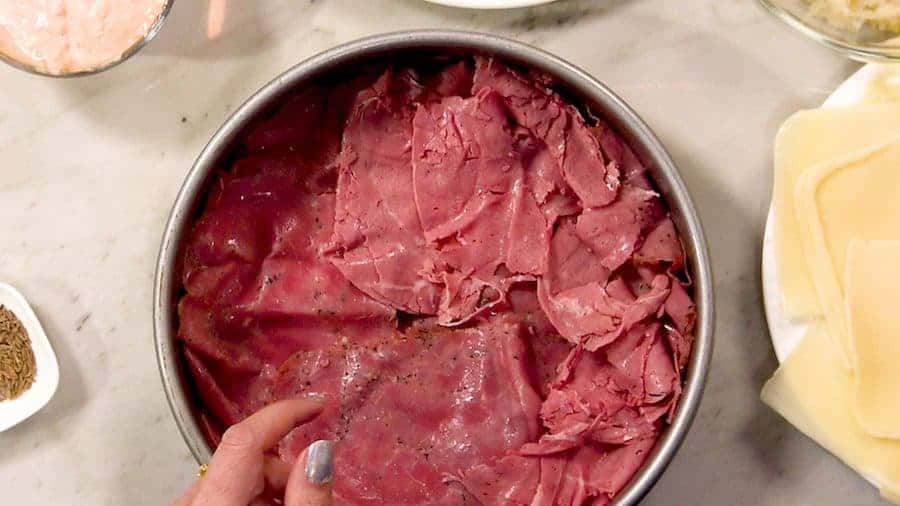 Layering pastrami and corned beef in a round cake pan.