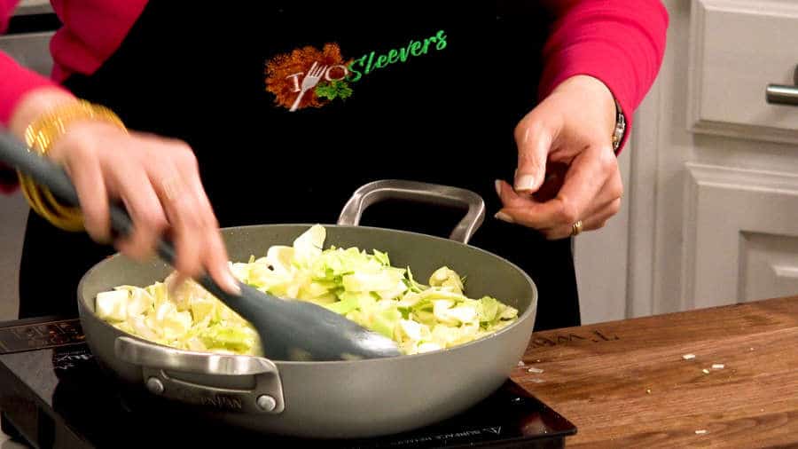 Side shot of stirring onions and cabbage in pan.