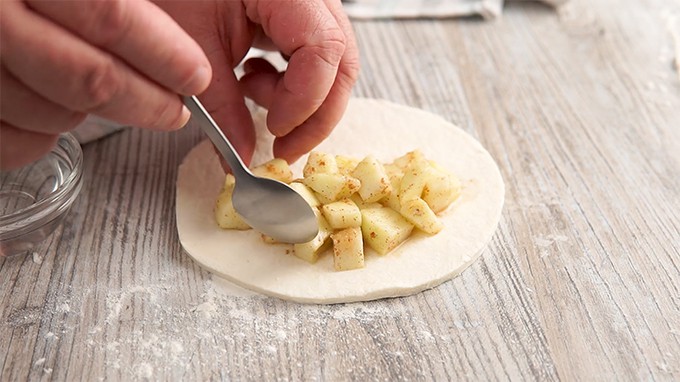 Placing apple fruit filling in the center of dough with a spoon