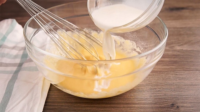 Milk being poured into a batter in a glass bowl.