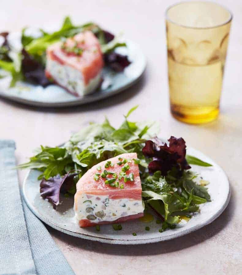 Two plates of Smoked Salmon and Cheese with a Glass of Water.