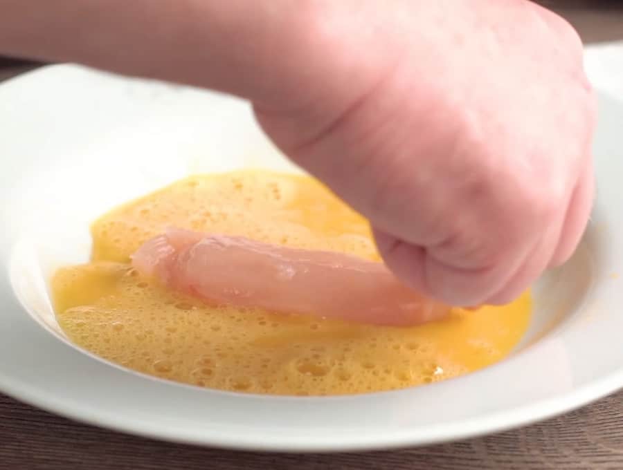 Side shot of dipping a chicken tender in the beaten egg.