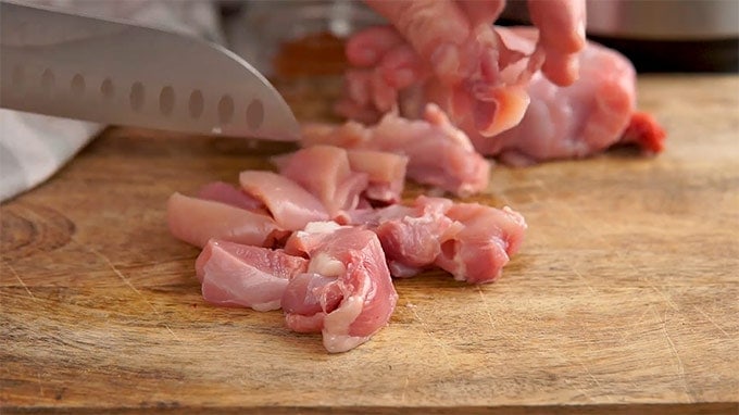 Chopped boneless skinless chicken thighs on a wooden cutting board for Chicken Taco Soup. 
