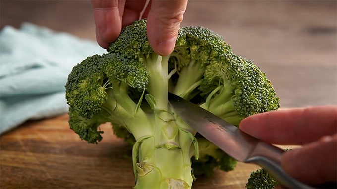 Side shot of chopping broccoli florets off of the stem.