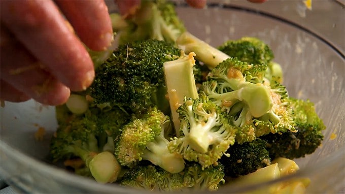 Side shot of hand tossing the broccoli in the sauce in a glass bowl.