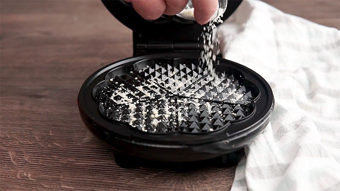 Side shot of Parmesan cheese being sprinkled into the waffle maker.