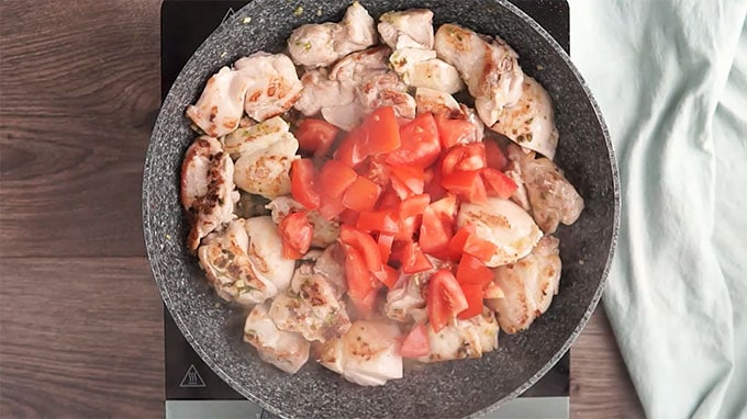 Overhead shot of diced tomatoes added to the pan with the chicken.