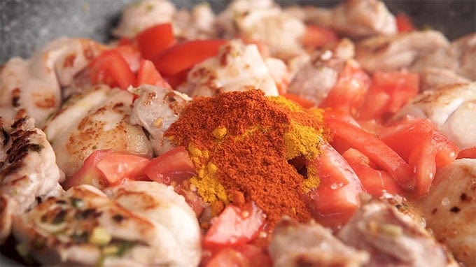 Side shot of the spices added to the pan with the chicken and tomatoes.
