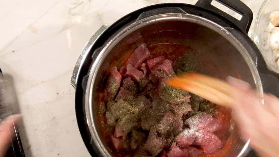 Overhead shot of mixing the beef, salt, pepper and herbs in the Instant Pot.